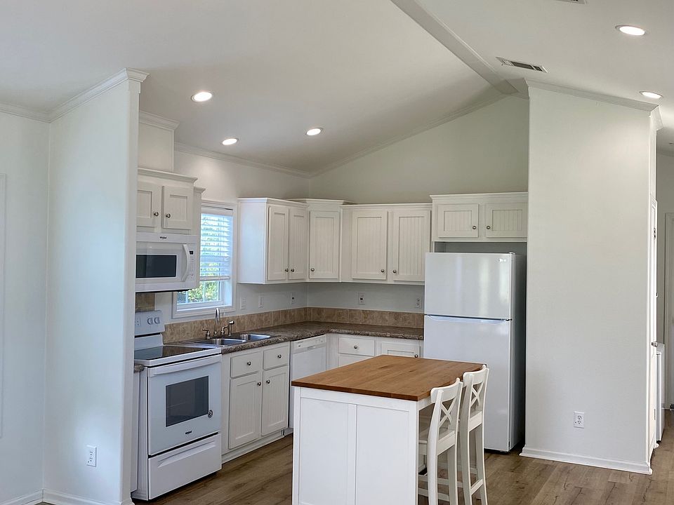 Kitchen featuring white appliances, wood counters, white cabinetry, lofted ceiling, and wood finished floors. The island is great for prepping food or enjoying a quick meal. Fridge included.