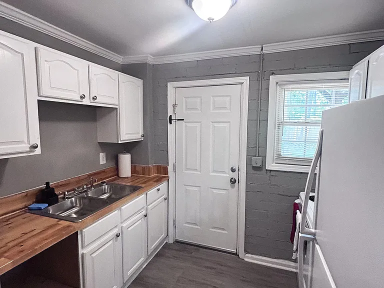 Efficient kitchen with ample white cabinetry, butcher-block style counters, and a double-basin sink plus a window for dayligh