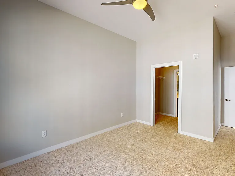 Spacious apartment bedroom with large closet, attached bathroom and plush carpet flooring.