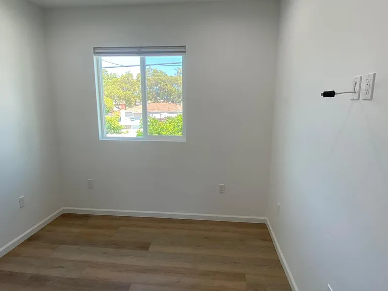 Well-lit bedroom with large window, great lighting, wood flooring, and flexible wall space for furniture placement.