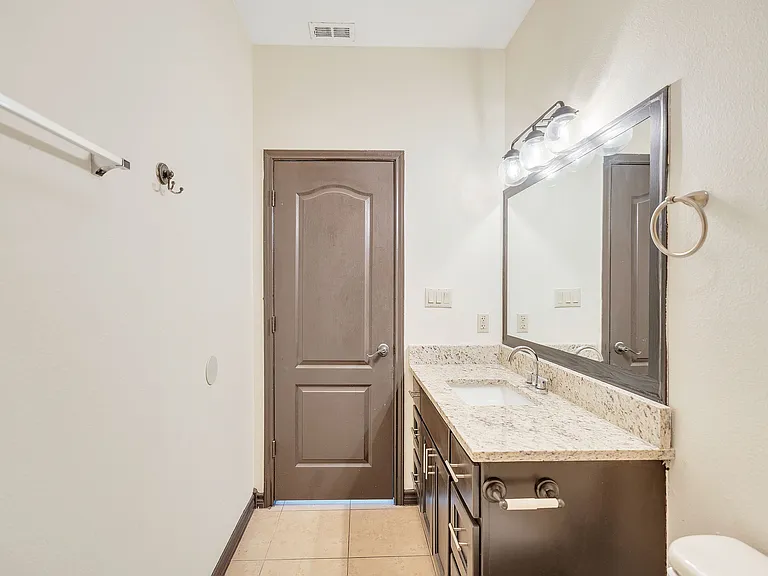 Bathroom at Merida Vista Apartments in Laredo, Texas, with a sink, toilet, and a large mirror above the sink