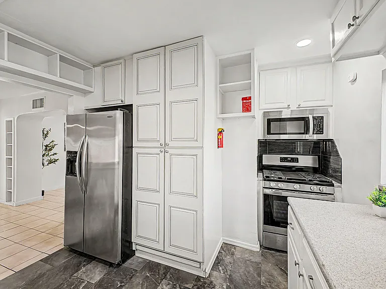 Efficient kitchen with abundant cabinetry, stainless steel refrigerator, gas range with built-in microwave, and durable count