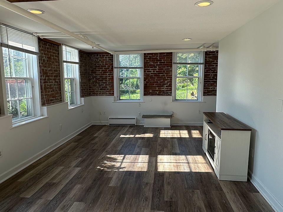 Large sunny living room with exposed brick walls and 4 full size windows.