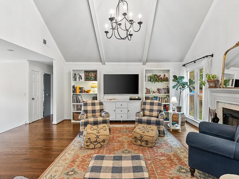 Spacious and bright living room with vaulted, beamed ceilings, a Smart TV, a fireplace, and windows looking out to the wooded backyard.