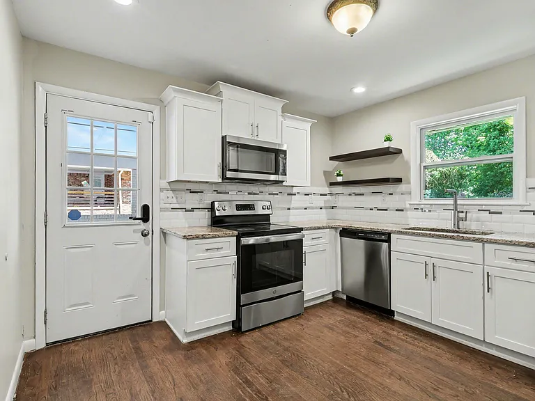 Updated kitchen with white cabinetry, stone-look counters, stainless appliances, and a large window over the sink.