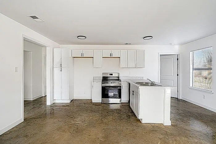 A modern, open-concept kitchen featuring crisp white cabinetry, a functional island, and industrial-style polished concrete floors.