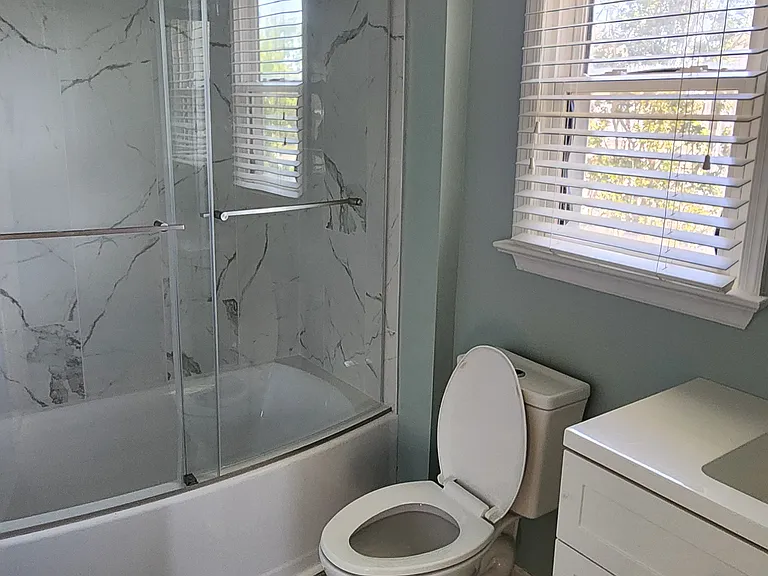 Newly renovated bathroom in bedroom 1 with new tile walls, tub, glass door and new vanity