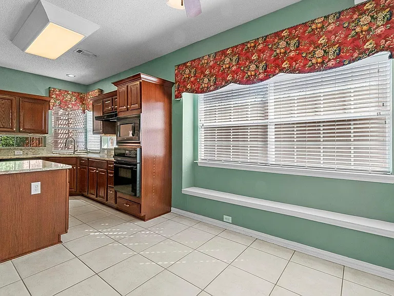 Kitchen featuring a central island with a light-toned countertop, wood cabinetry, built-in appliances, and tile flooring