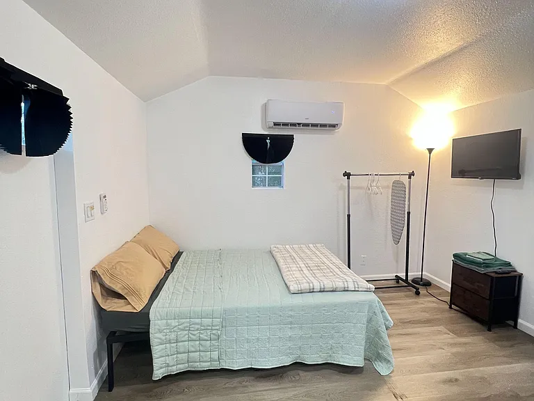 Furnished bedroom with vinyl plank flooring, wall-mounted TV, mini-split A/C, and a clothing rack for added storage.