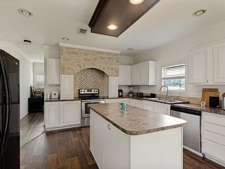 Spacious kitchen with center island, ample white cabinetry, stainless appliances, and a window over the double sink.