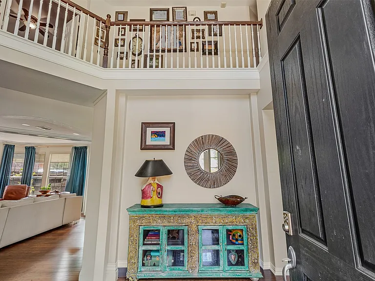 Two-story foyer with a dark wood-finish entry door, a second-story interior balcony with white balusters and a wood-finish handrail, and wood-finish flooring