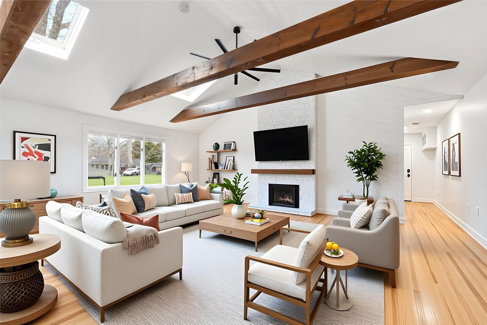  Vaulted ceiling living area featuring exposed wood beams, dual skylights, a white brick fireplace.