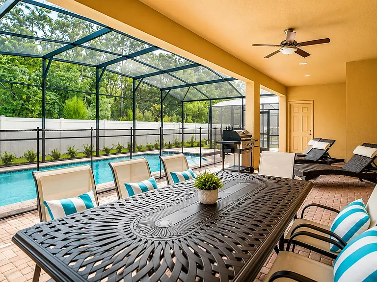 Covered screened patio with a dining table, lounge chairs, and ceiling fan, opening to a private pool and fenced yard.