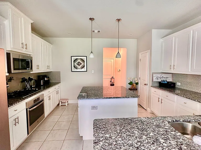 Spacious kitchen with granite countertops, large island seating, ample white cabinetry, and stainless-steel appliances.