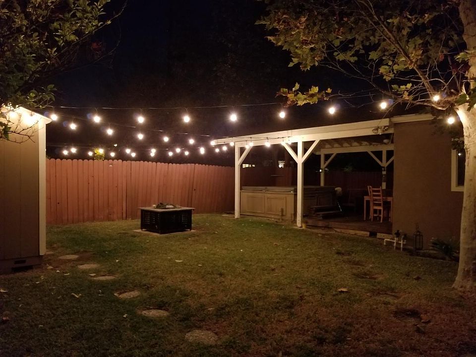 Backyard has string lights, shed, and fire pit.