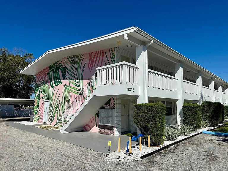 Charming apartment building with vibrant tropical mural, white modern architecture, and lush greenery, perfect for stylish living.