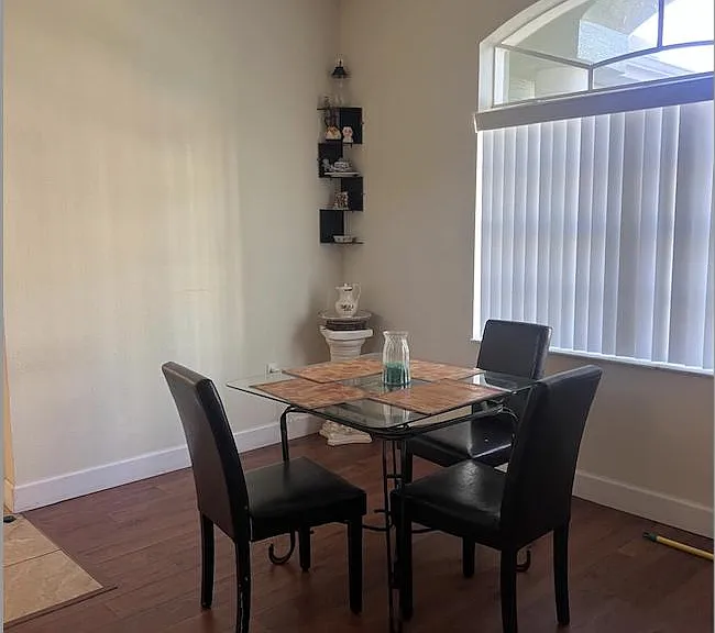 Dining area with a glass-top table for four, hardwood-style flooring, and an arched window bringing in natural light.