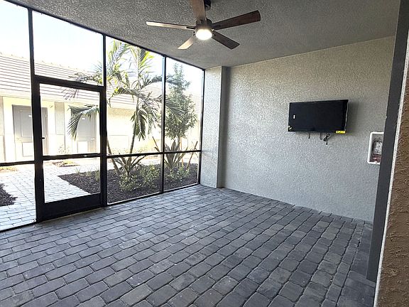 Expansive front screened lanai with ceiling fan and wall-mounted TV. An ideal space for outdoor dining or entertaining.