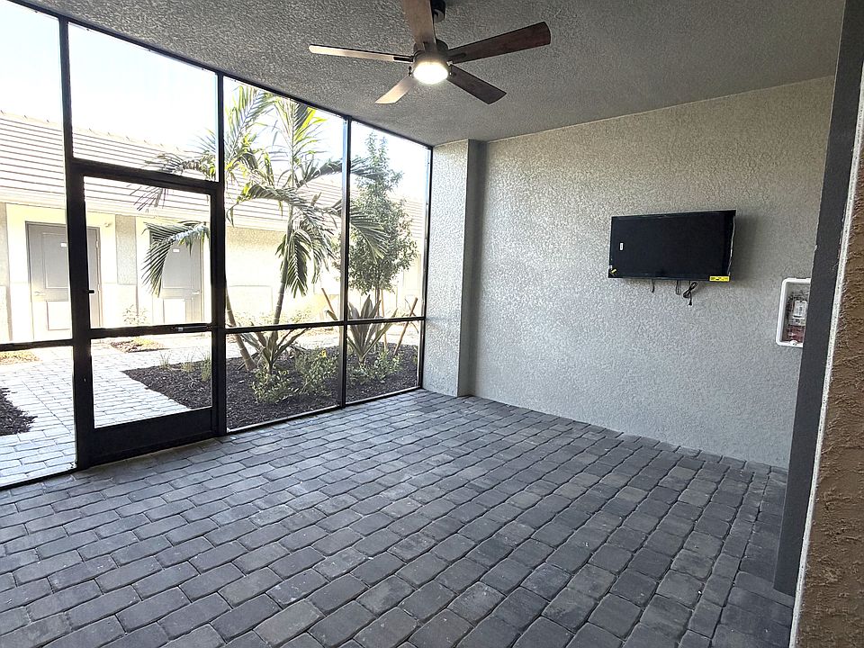 Expansive front screened lanai with ceiling fan and wall-mounted TV. An ideal space for outdoor dining or entertaining.