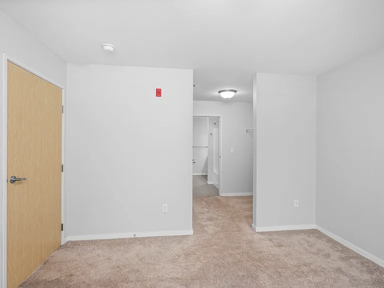 Bright, carpeted room with a modern wooden door and inviting hallway leading to a restroom, ideal for cozy and comfortable living. Bright, carpeted room with a modern wooden door and inviting hallway leading to a restroom, ideal for cozy and comfortable l
