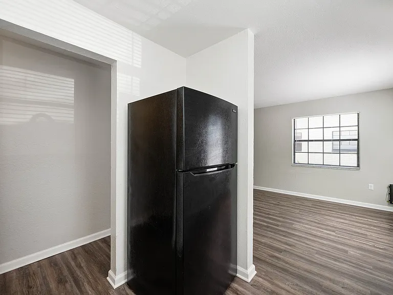 Modern apartment corner featuring a sleek black refrigerator, stylish hardwood flooring, and an inviting natural light-filled space with large windows.