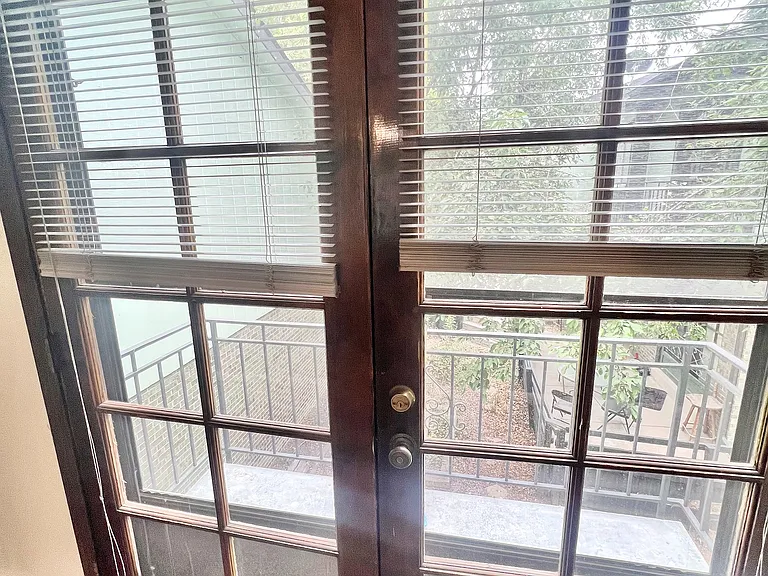 Charming glass French doors with elegant blinds opening to a private balcony surrounded by lush greenery.