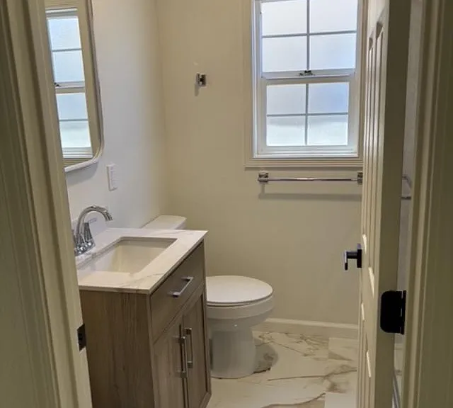 Hallway view of entirely renovated bathroom, including new walk-in shower, new toilet, cabinet, light features and gorgeous new tile floor.