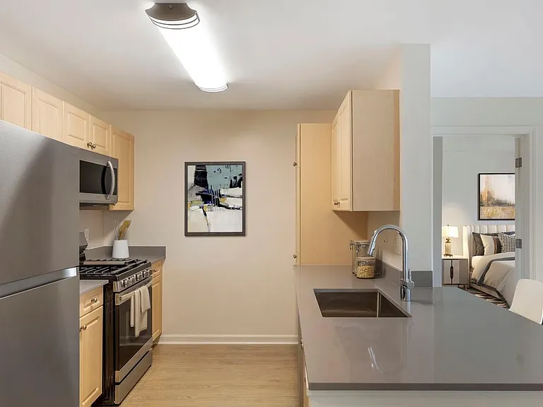 Phase I Renovated Package I apartment kitchen with stainless steel appliances, grey quartz countertops, oak cabinetry, and hard surface flooring