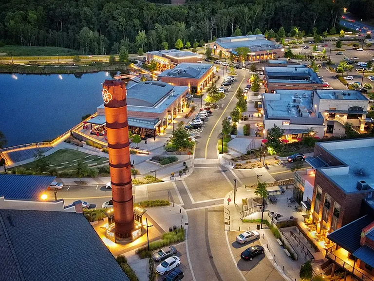 Aerial view of a vibrant shopping center by the lake at dusk, featuring well-lit pathways and modern architecture.