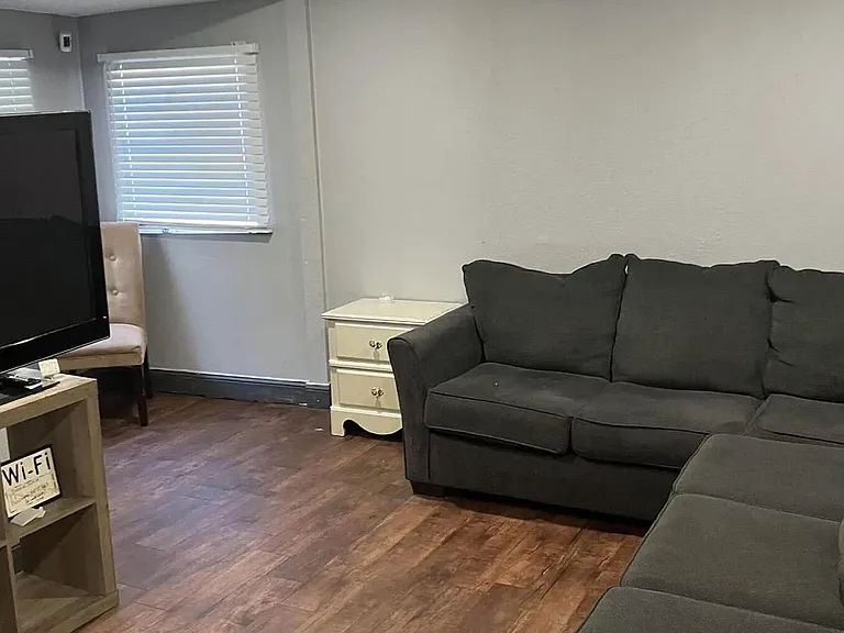 Comfortable living area with sectional seating, TV setup, and durable wood-look flooring with window blinds for light control
