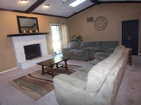 Spacious great room features wood-burning fireplace, vaulted ceilings w/wood beams, 2 skylights, & sliding door to back deck.