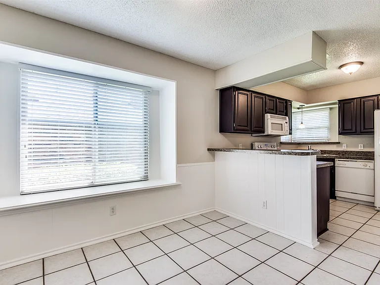 Kitchen and dining area featuring dark wood cabinetry, light-toned countertops, and white appliances