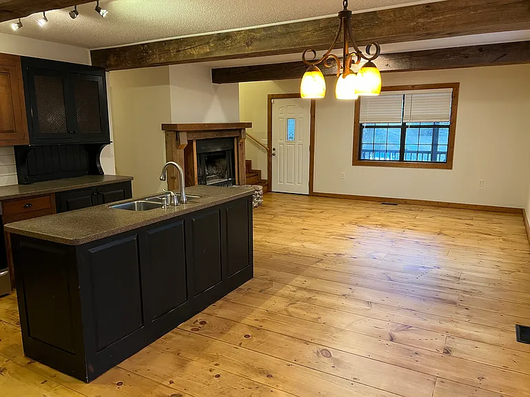 View of downstairs shared space from dining area. Living room is furnished with seating area (couch, table, lamp, rocking chair), and large Roku T.V.