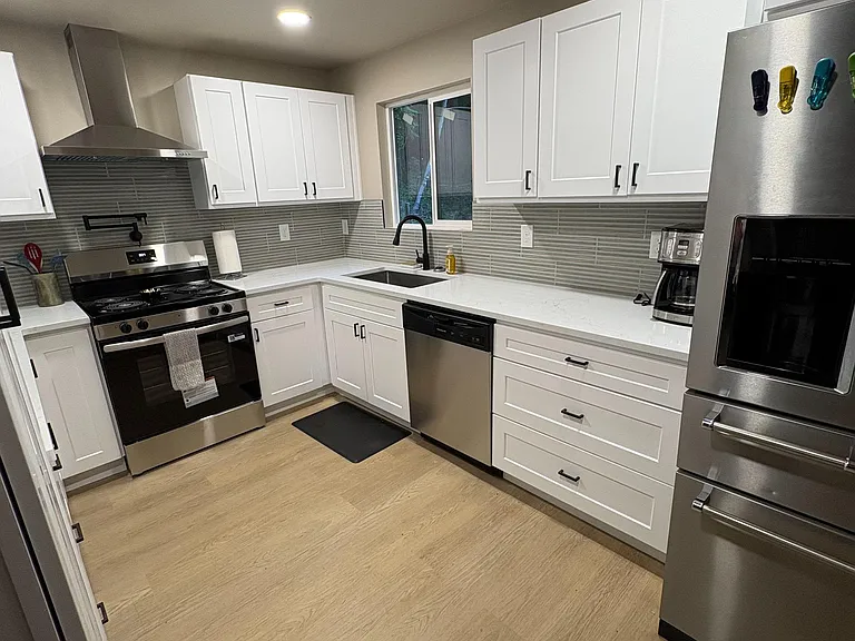Updated L-shaped kitchen with shaker cabinets, stainless steel appliances, and generous counter space with window over sink.