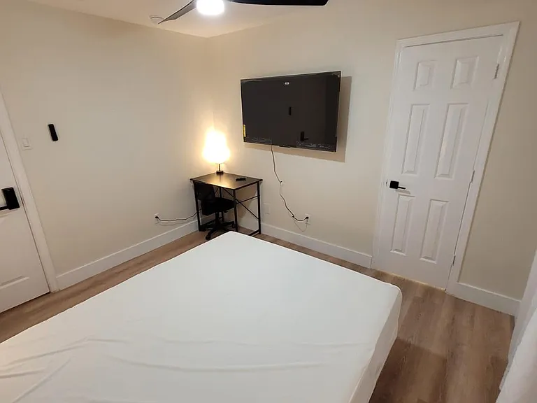 Private bedroom with ceiling fan, wall-mounted TV, and dedicated desk area, plus durable wood-look flooring.