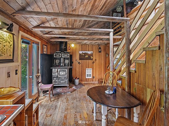 This view from the kitchen is of the dining area and its antique wood-fired cookstove.  At left are the French doors which open out onto the the spacious deck.  The stairway at right leads up the the loft/living room and ensuite bedroom beyond.>