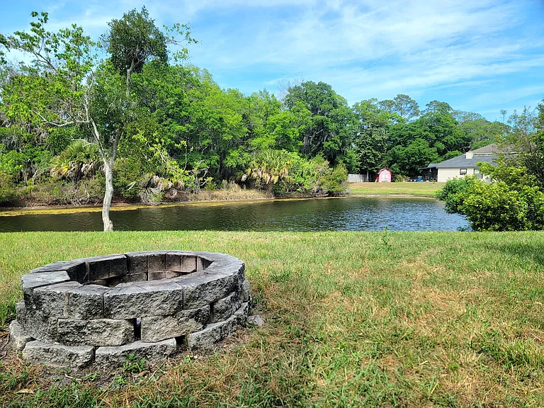 Private backyard with a stone fire pit and a peaceful pond view.