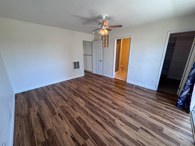 Primary bedroom with walk-in closet, full bathroom, ceiling fan and wall heater.