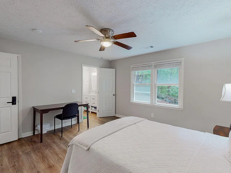 Spacious bedroom with a ceiling fan, large window for natural light, and a dedicated desk area for work or study.