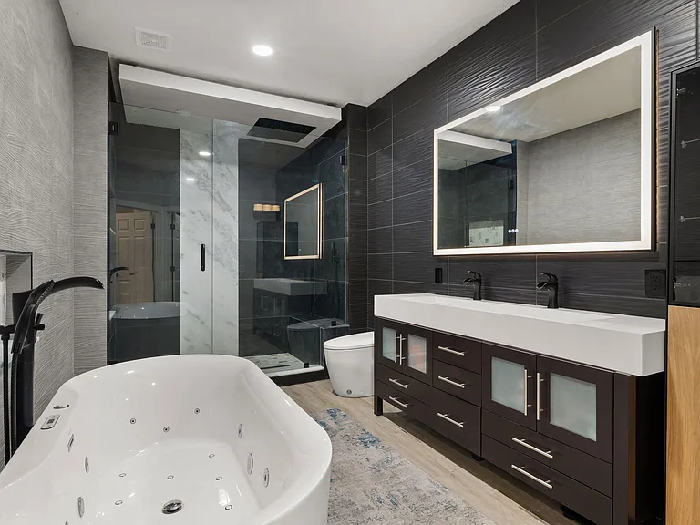 Spa-style bathroom with soaking tub, glass-enclosed shower, and double-sink vanity with ample storage and a lit mirror.