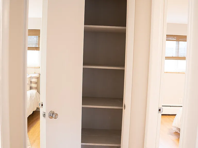 Bright hallway showcasing a clean built-in linen closet with ample shelving, surrounded by warm hardwood flooring and soft natural light.