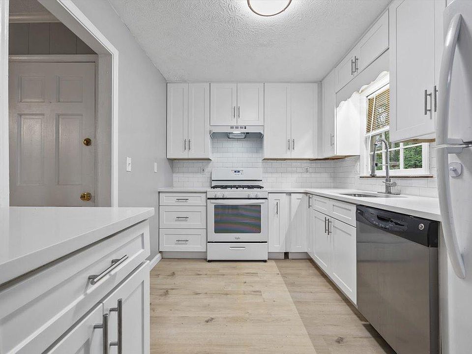 Updated galley kitchen with ample white cabinetry, subway-tile backsplash, dishwasher, and window over the sink.