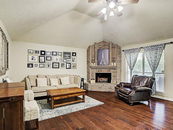 Beautiful living room with hardwood floors, soaring ceilings, and a brick fireplace.