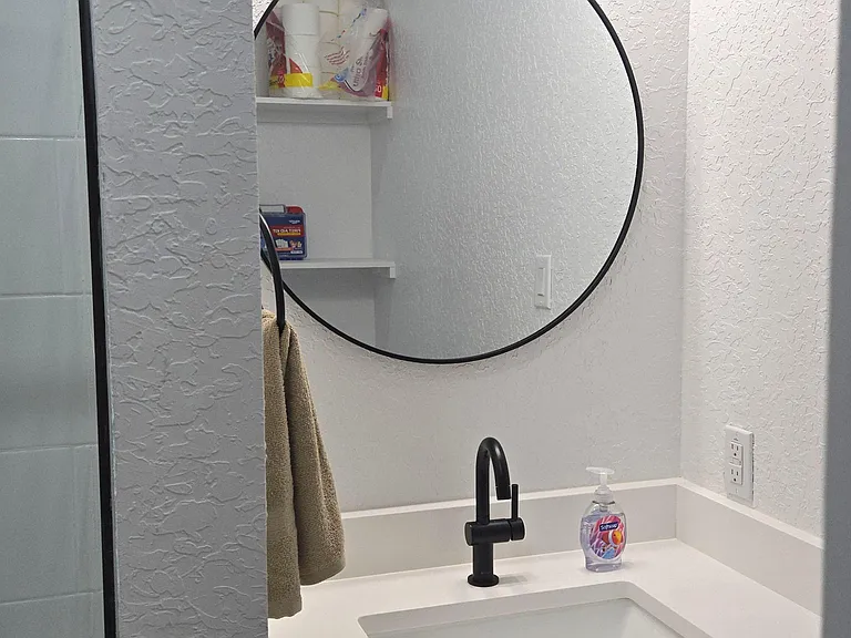Room 1 updated bathroom vanity with a solid-surface countertop, undermount sink, matte black faucet, and round mirror.