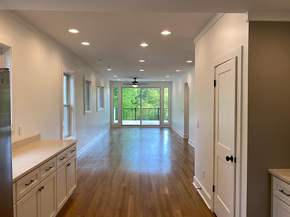 From the Kitchen, look out through the dining room and the living room onto the back deck which looks onto green trees.