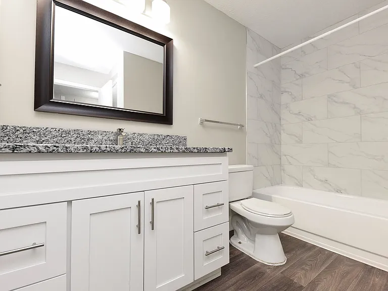 Bright bathroom with granite counters and bathtub with marble backsplash