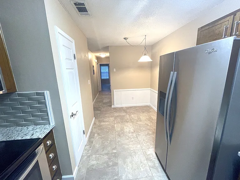 view of the fridge, eating area and the pantry door. There is also a view of the hallway, guest bedroom door and the master bedroom at the end of the hallway.
