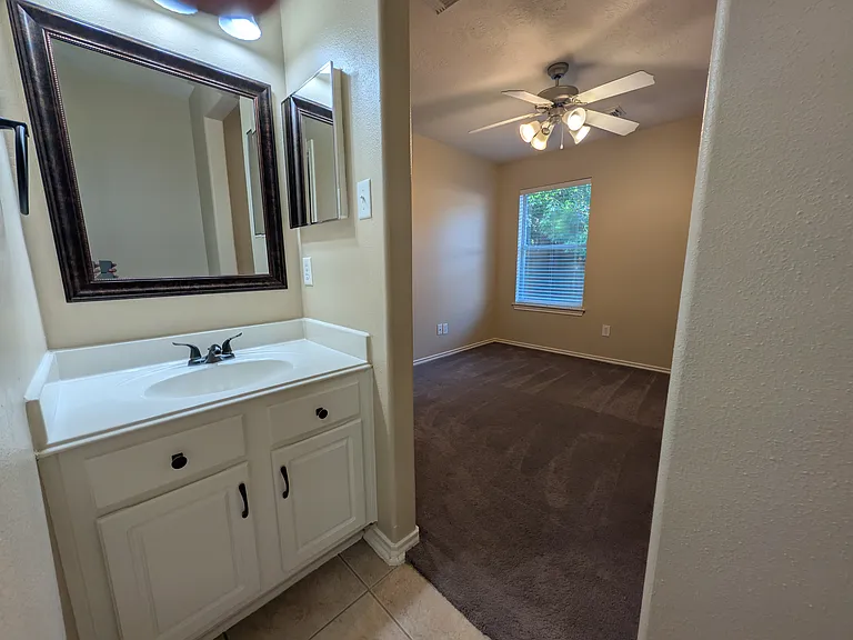 Private single vanity area connected directly to Bedroom 2, complete with updated fixtures, framed mirror, and cabinet storage.