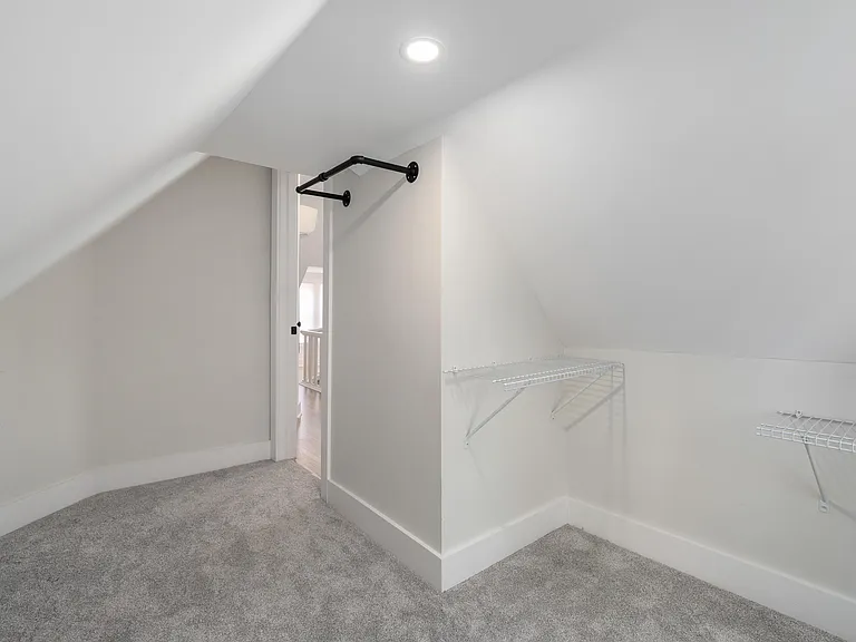 Finished walk-in closet with sloped ceilings, carpet flooring, and built-in wire shelving for organized storage.