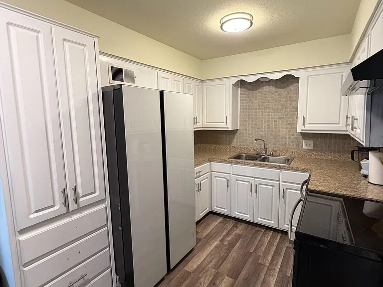 Functional kitchen with ample white cabinetry, generous counter space, tile backsplash, and a double-basin sink.